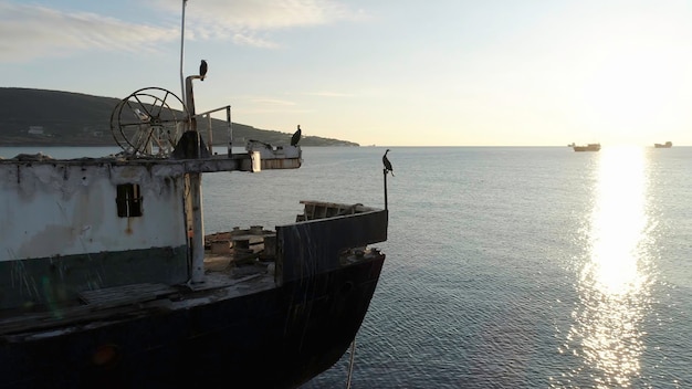 Foto nahaufnahme eines alten und zerbrochenen schiffes, das in der nähe der küste vor dem wunderschönen sonnenuntergang am himmel steckt.