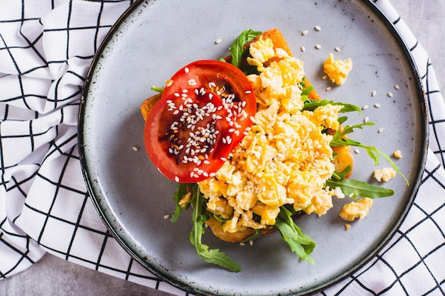 Nahaufnahme eines appetitlichen Toasts mit Rührei, Tomaten und Sesamkörnern auf einem Teller von oben