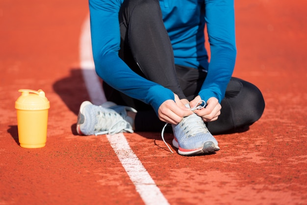 Foto nahaufnahme, eines athleten, der seine schnürsenkel bindet. bemannen sie das festziehen seiner schnürsenkel, die aus den grund auf einer laufbahn sitzen.