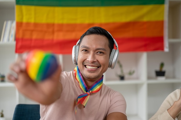 Nahaufnahme eines attraktiven und glücklichen asiatischen schwulen Mannes mit Kopfhörern, der das LGBT-Herz hält