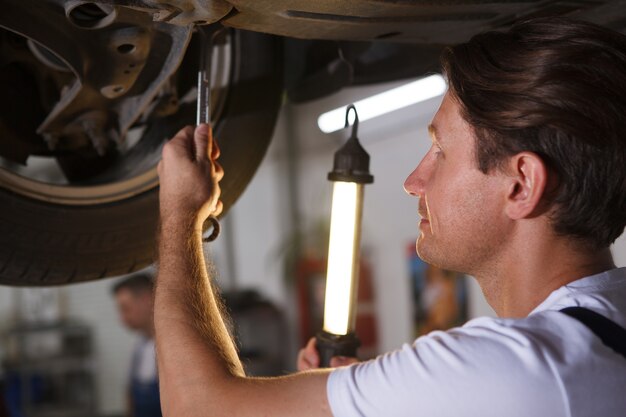 Nahaufnahme eines Automechanikers, der eine Lampe hält und das Rad eines Autos auf dem Autolift repariert