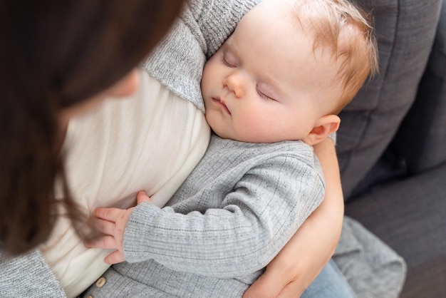 Nahaufnahme eines Babys, das zu Hause in den Armen der Mutter schläft, glückliches Mutterschaftskonzept