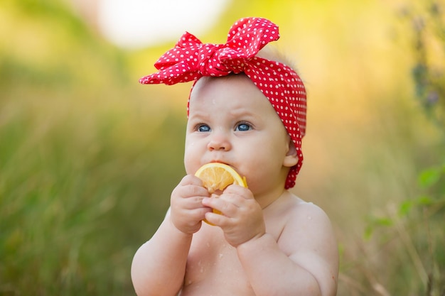 Nahaufnahme eines Babys in einem roten Stirnband isst eine Orangenscheibe im Freien gesunder Snack für Kinder