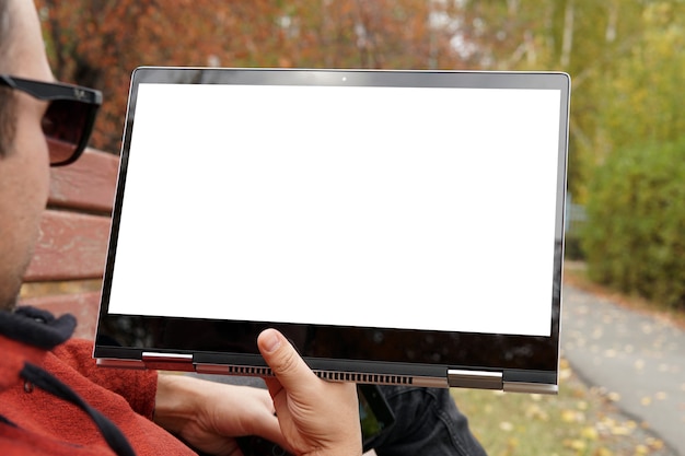 Nahaufnahme eines beiläufig gekleideten jungen Mannes mit moderner digitaler Tablette beim Sitzen im Park, Sonnenlicht. Leerer weißer Bildschirm. Der junge Mann liegt im Park auf einer Bank und sieht sich ein Video auf dem Computer an. Attrappe, Lehrmodell, Simulation