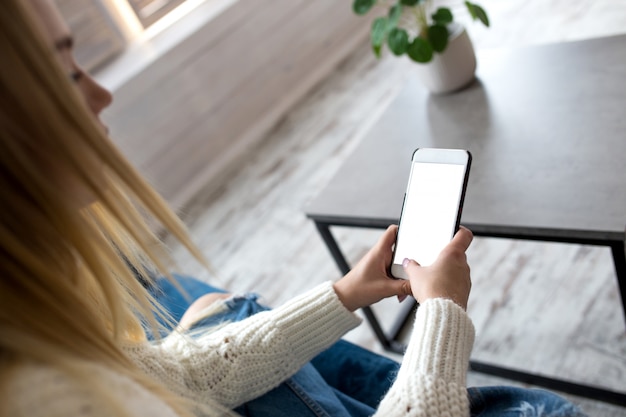 Nahaufnahme eines blonden Sitzens auf einem Sofa mit einem Smartphone.