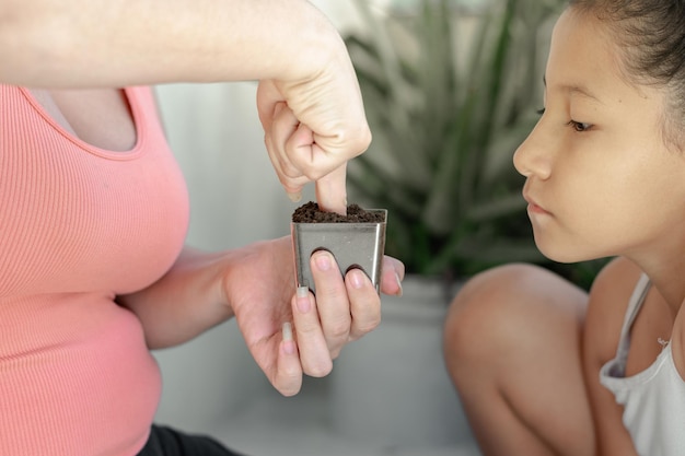 Nahaufnahme eines braunhäutigen Latina-Mädchens, das aufmerksam zusieht, wie ihre Mutter ihr beibringt, wie man eine Pflanze pflanzt