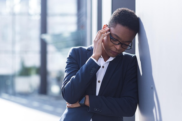 Nahaufnahme eines Büroangestellten, der müde und überarbeitet ist und starke Kopfschmerzen und Depressionen hat. Eine afroamerikanische Frau außerhalb des Büros hat schlechte Nachrichten erhalten