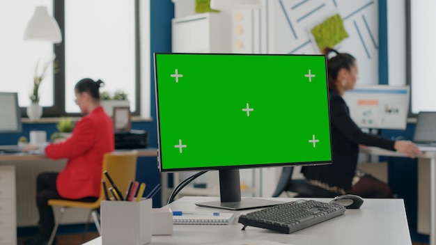 Nahaufnahme eines Computers mit isoliertem grünem Bildschirm am leeren Schreibtisch, Mock-up-Vorlage mit Kopienraum-Chroma-Key im Geschäftsbüro. Chromakey-App auf Monitoranzeige im Startbereich.