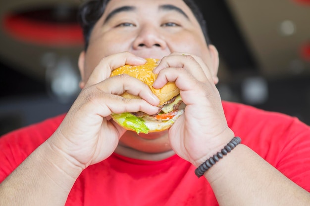 Nahaufnahme eines dicken asiatischen Mannes, der einen Cheeseburger isst