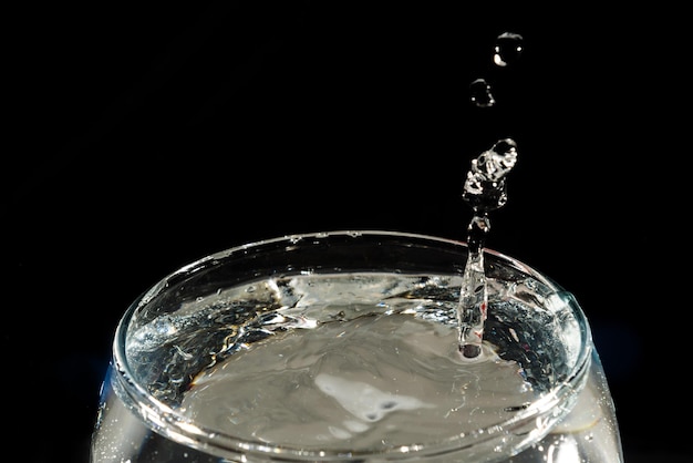 Foto nahaufnahme eines durchsichtigen glasbechers mit wasser im inneren und tropfen, die einen spritz machen