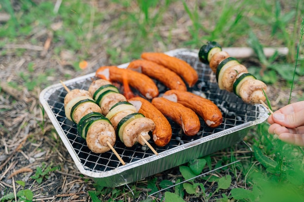 Nahaufnahme eines Einweggrills für ein Picknick im Freien mit Gemüse auf einem Holzstab