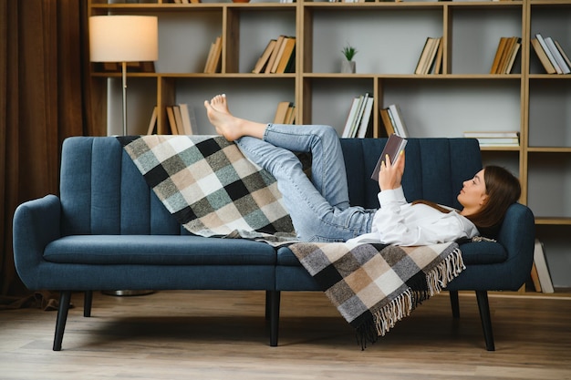 Nahaufnahme eines entspannten Mädchens mit einem Smartphone, das zu Hause auf einem Sofa im Wohnzimmer liegt