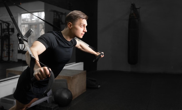 Nahaufnahme eines fitten Mannes, der im Fitnessstudio auf dem Simulator trainiert und die Muskeln der Arme und des Rückens schüttelt, während er Übungen eines jungen Athleten macht