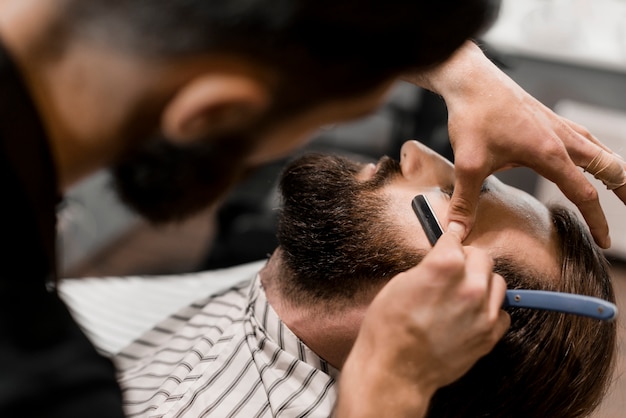 Nahaufnahme eines Friseurs, der das Haar des Mannes mit Rasiermesser schneidet