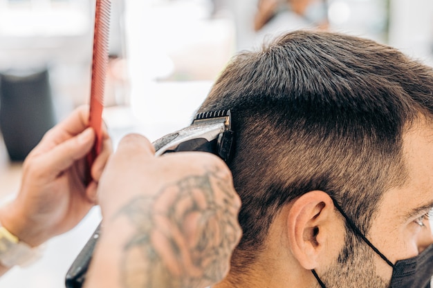 Nahaufnahme eines Friseurs, der einem kaukasischen Mann mit einer Maschine und einem Kamm in einem Salon die Haare schneidet