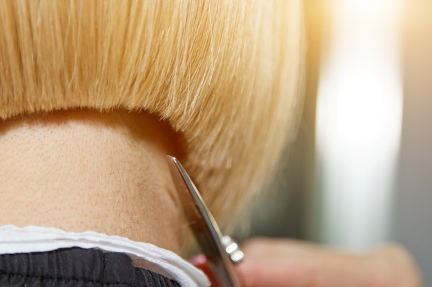 Nahaufnahme eines Friseurs schneidet nasses weißes Haar eines Kunden in einem Salon. Friseur schneidet eine Frau. Seitenansicht einer Hand, die Haar mit einer Schere schneidet.