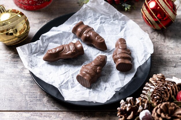 Nahaufnahme eines fröhlichen, eingewickelten Schokoladen-Weihnachtsmanns auf einem Holztisch