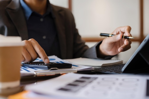 Nahaufnahme eines Geschäftsmannes, der an einem Taschenrechner arbeitet, um Finanzdaten zu berechnen, Berichtbuchhaltungsdokument und Laptop-Computer im Bürogeschäftskonzept