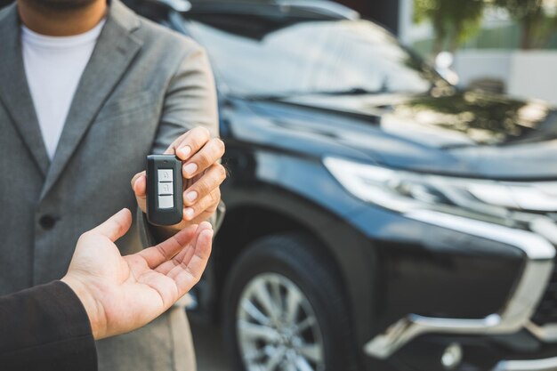 Nahaufnahme eines Geschäftsmannes im Anzug, der seine Hände zeigt oder Autoschlüssel für Kunden gibt, die ein neues Auto bekommen. Mietwagenkonzept kaufen und verkaufen.