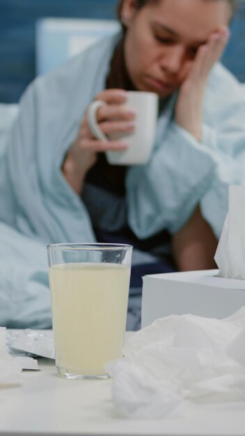 Nahaufnahme eines Getränks mit sprudelndem Vitamin und Wasser im Glas auf dem Tisch mit Medikamenten und Geweben. Frau mit Krankheit, die sich darauf vorbereitet, medizinisches Getränk gegen Erkältung und Grippe zu nehmen.