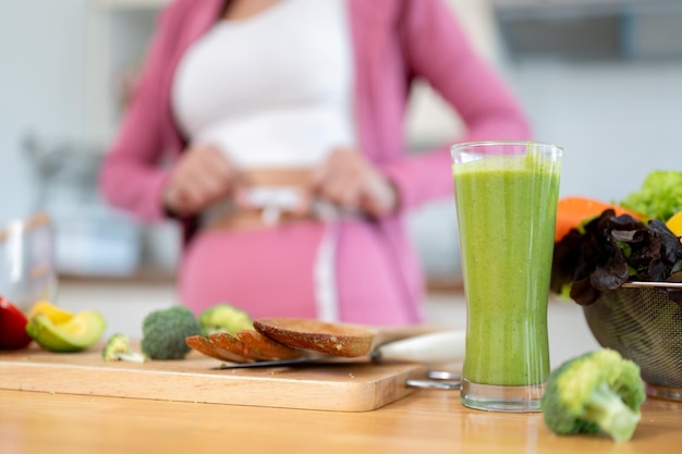 Nahaufnahme eines Glases gesunden grünen Smoothie und frischem Gemüse auf einem Tisch in der Küche