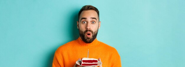 Foto nahaufnahme eines glücklichen erwachsenen mannes, der seinen geburtstag feiert, geburtstagskuchen mit kerze hält und wünsche macht