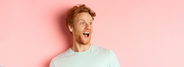 Foto nahaufnahme eines glücklichen und faszinierten jungen mannes mit roten haaren, der sich das promo-angebot ansieht und mit a nach links schaut