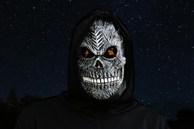 Foto nahaufnahme eines grim reaper-mannes in einer todesmaske mit feuerflammen in den augen am sternenreichen nachthimmel