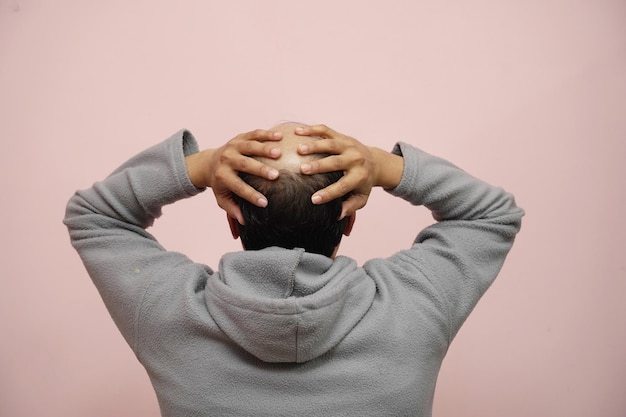 Nahaufnahme eines halbkahlköpfigen Mannes, der seinen Kopf hält, während er einen Hoodie mit rosa Hintergrund trägt