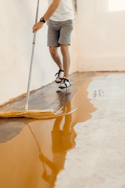 Nahaufnahme eines Handwerkers, der gelbe Flüssigfarbe auf einen neuen Boden aufträgt