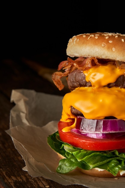 Nahaufnahme eines hausgemachten leckeren Burgers mit Zwiebelsalat, Cheddar-Käse, Speck und Tomate auf einem Holztisch mit Kopierraum