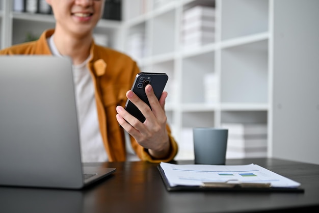 Nahaufnahme eines intelligenten jungen Geschäftsmannes, der während der Arbeit im Büro ein Smartphone benutzt