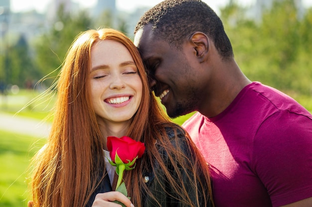 Nahaufnahme eines interrassischen Paares, das im Frühlingsherbstpark eine weiße Rose hält.