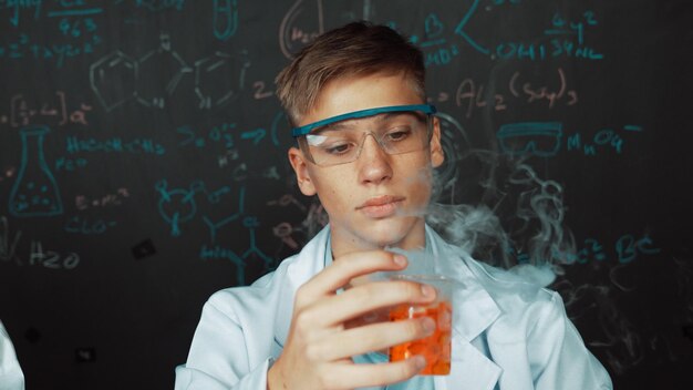 Nahaufnahme eines Jungen, der eine chemische Lösung untersucht, während er einen Becher hält