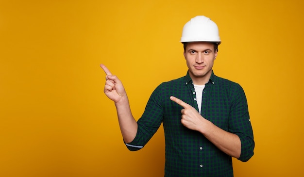 Nahaufnahme eines jungen glücklichen und selbstbewussten Vorarbeiters oder Architekten im Bauhelm posiert einzeln auf gelbem Hintergrund.