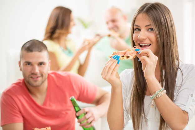 Nahaufnahme eines jungen Mädchens, das mit ihren Freunden im Hintergrund lächelt und Pizza isst.