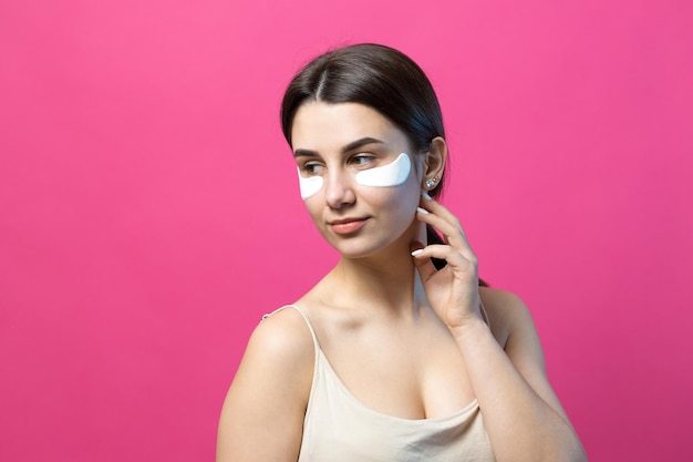 Nahaufnahme eines jungen Mädchens in einem hellen Top auf weißem Hintergrund, das ein Gesichts-Make-up macht