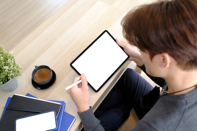 Nahaufnahme eines jungen Mannes, der auf Holzboden sitzt und ein digitales Tablet mit leerem Bildschirm hält.