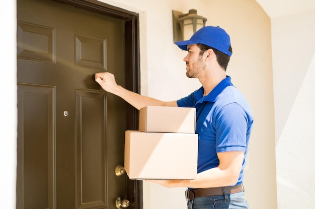Nahaufnahme eines jungen Mannes, der ein paar Pakete an ein Haus liefert und an dessen Tür klopft