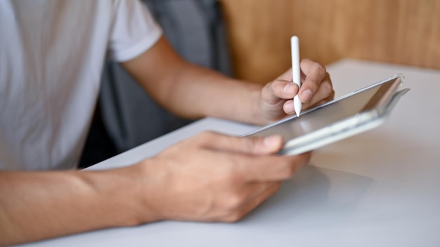 Nahaufnahme eines jungen Mannes, der in einem Café arbeitet, während er die Seitenansicht eines digitalen Tablets verwendet