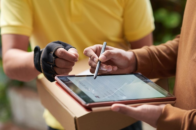 Nahaufnahme eines jungen Mannes, der nach Erhalt des Pakets ein Dokument auf einem Tablet-Computer unterzeichnet