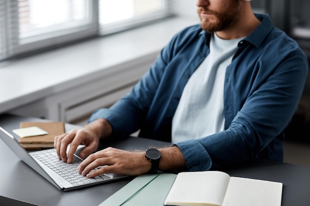 Nahaufnahme eines jungen Mannes in Freizeitkleidung, der auf einer Laptoptastatur tippt