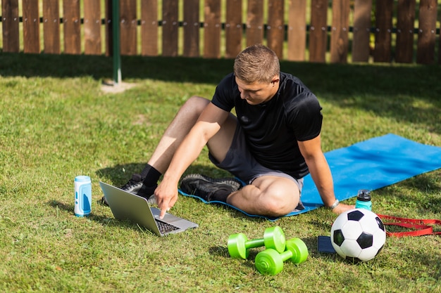 Nahaufnahme eines jungen Mannes in Sportuniform ruht auf Rasen im Garten, schaut sich einen Film an und studiert