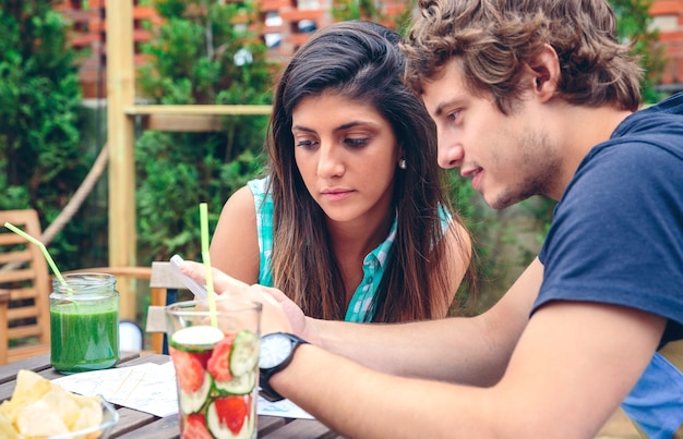 Nahaufnahme eines jungen paares, das smartphone an einem sommertag im freien mit gesunden getränken am tisch sitzt?