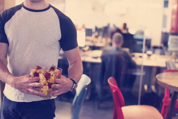 Nahaufnahme eines jungen Softwareentwicklers, der im Startup-Büro einen Obstsalat aus einer durchsichtigen Tasse isst