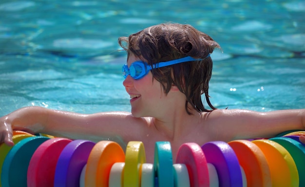 Nahaufnahme eines Kindes mit Wassergläsern im Pool, das auf einer Boje ruht