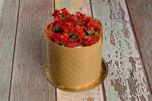 Nahaufnahme eines Kleidkuchens, eingewickelt in eine strukturierte Schicht aus gesalzenem Schokoladenkaramell, mit Erdbeeren und roten Kalanchoe-Blumen.