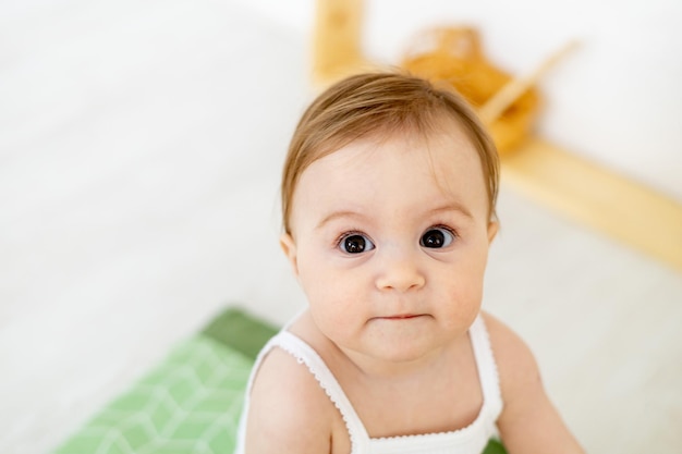 Nahaufnahme eines kleinen Babys zu Hause in einem hellen Kinderzimmer mit großen braunen Augen