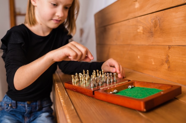 Nahaufnahme eines kleinen blonden Mädchens, das auf einem Brett sitzt und Schach spielt