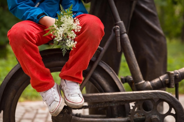 Nahaufnahme eines kleinen Jungen mit wilden Blumen, der draußen auf einem Metallfahrrad auf natürlichem Hintergrund sitzt